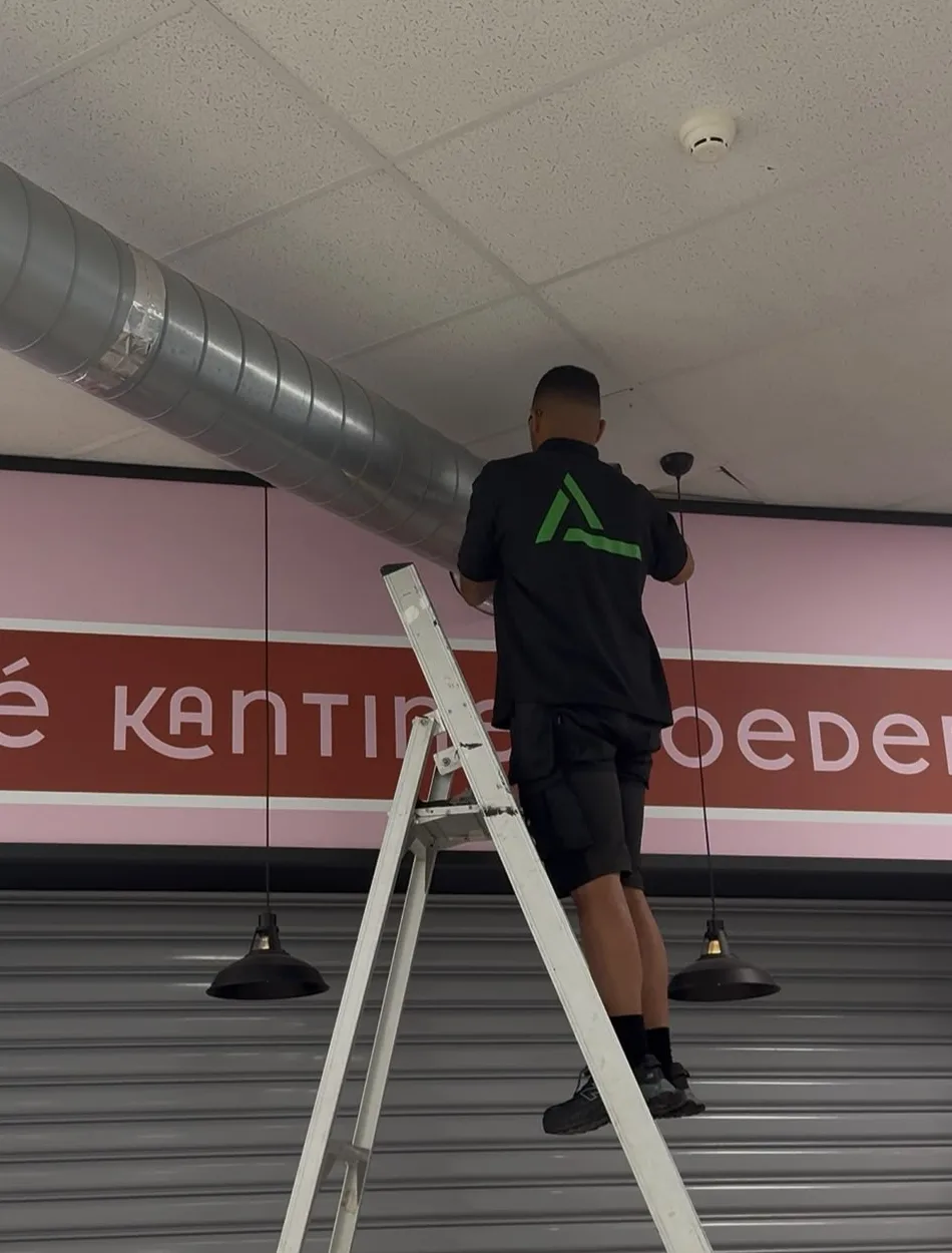 Monteur van All Ventilatie werkt vanaf een ladder aan een luchtkanaal